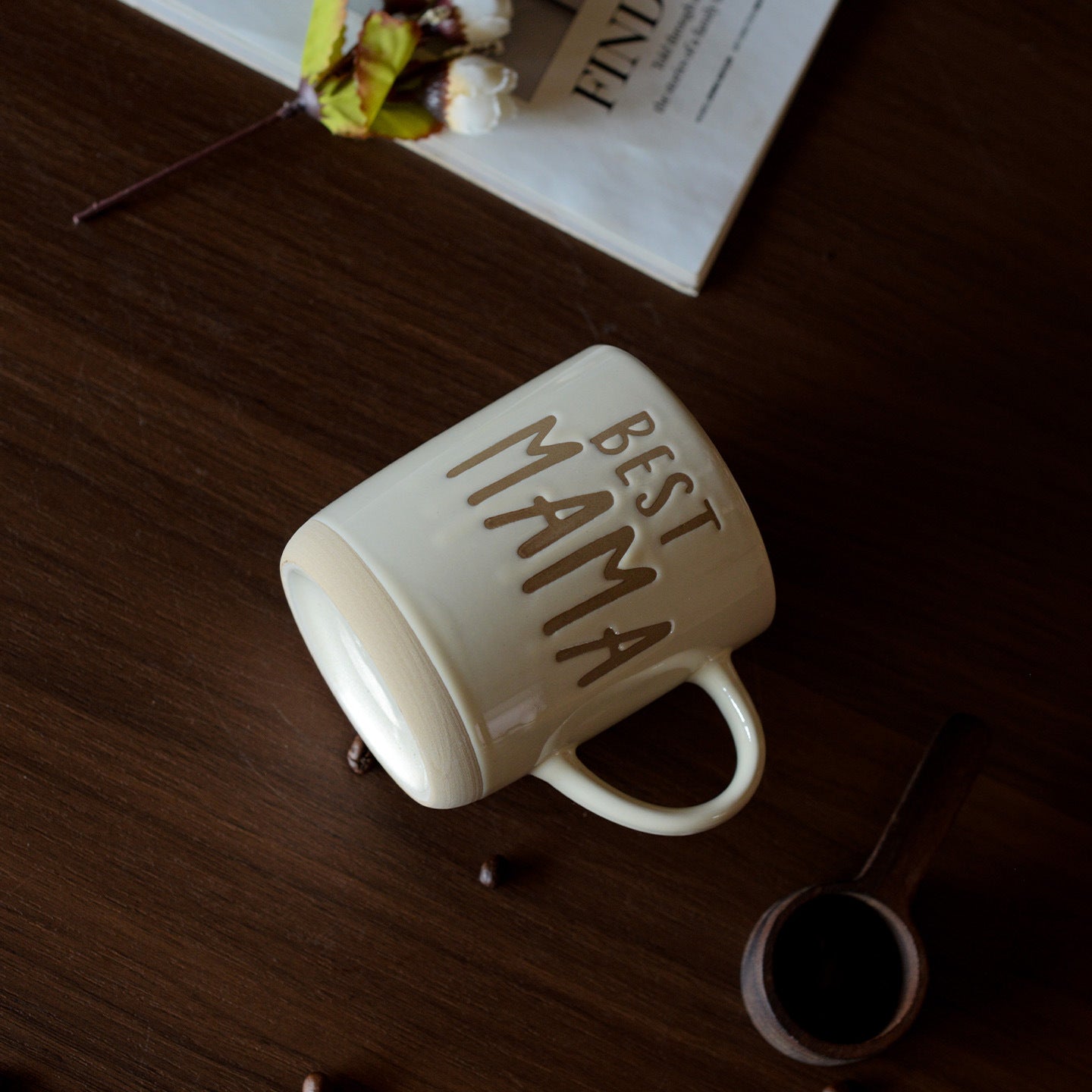 A beige mug with 'Best Mama' text lay flat on a wooden surface